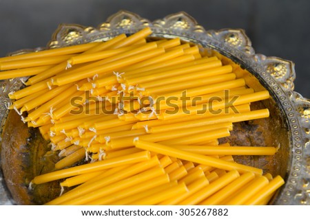 Stack of bright yellow candles ready for offering on a silver tray at a Buddhist temple in Bangkok Thailand