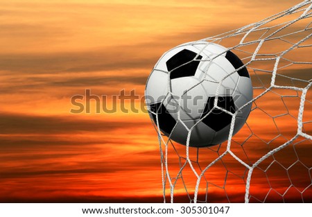 Symbolic of success and victory for classic soccer ball (football) have black and white color going into the in-goal net after shot in the game with a  sky background. success concept