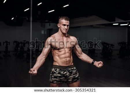 Beautiful sport bodybuilder man on a diet, weight training with dumbbells pumping muscle.With six pack, perfect brakes, shoulders, biceps, triceps and chest.Young adult doing weight lifting at the gym