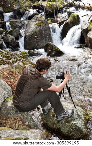 A tourist is taking photo near the small fall of the mountain stream in the spring Pyrenees.