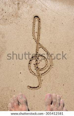 Concept, conceptual music symbol handwritten in sand on a beach background with feet in an exotic island for tropical, summer, sea, ocean, calendar, travel, holiday, sunny, tourism, resort, time relax
