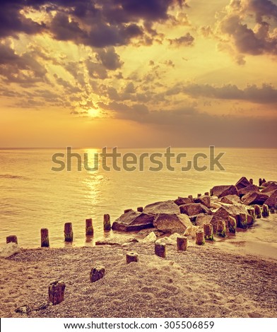 Retro toned dramatic sunset over beach and rocky pier.