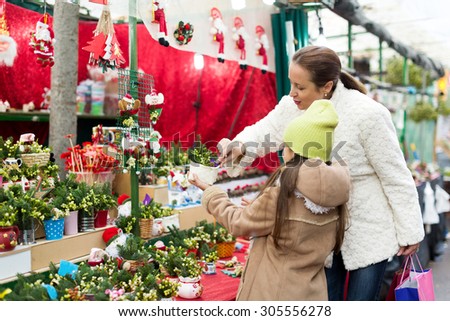 Smiling woman with her daughter buying Christmas floral composition with mistletoe  in market. Focus on woman