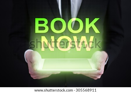 Businessman holding a tablet pc with "book now" text on virtual screen. Business concept. Internet concept.