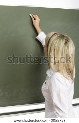 Woman (teachear) are standing with chalk in hand close to greenboard. She's starting to write. Focus on board/hand.