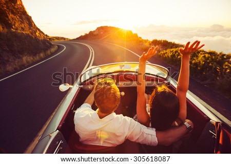 Happy Couple Driving on Country Road into the Sunset in Classic Vintage Sports Car  Royalty-Free Stock Photo #305618087