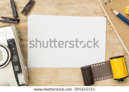 Blank paper with photo film in cartridge and film camera on wooden table.