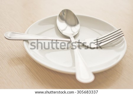 Plate isolate with spoon and fork on a wooden table . (Focus at fork and spoon in cross position)