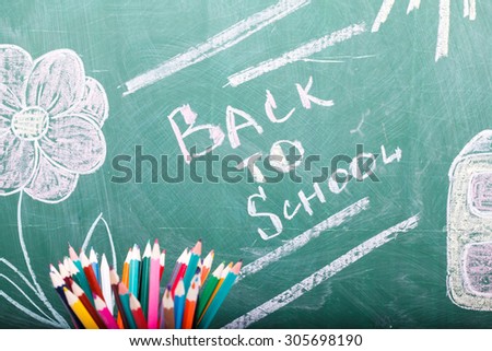 Colorful pencils of red yellow orange violet purple pink green and blue in stationary cup on written with chalk back to school on blackboard background copyspace, horizontal picture