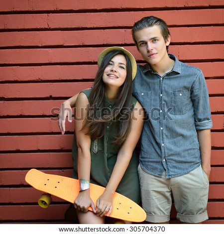 Young couple posing with penny board summer outdoor against red brick wall. Urban lifestyle, happiness, joy, friends, teenage, first love concept. Image toned and noise added.