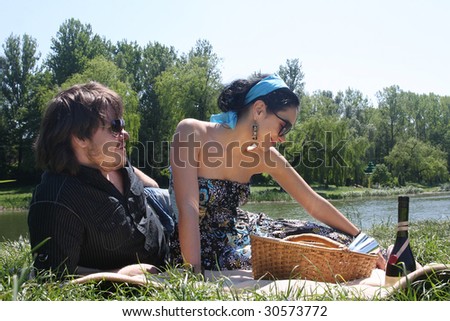Couple sitting together by a lake with a picnic basket.