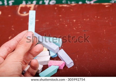 Human hand holding one blue chalk and heap of colorful pieces  pastel pink violet green blue yellow white colors lying on old brown school table copyspace, horizontal picture
