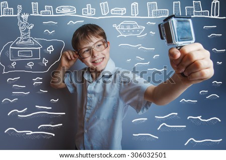 a boy of 10 years of European appearance with glasses holding a camera in the hands of the self on a  gray  background
