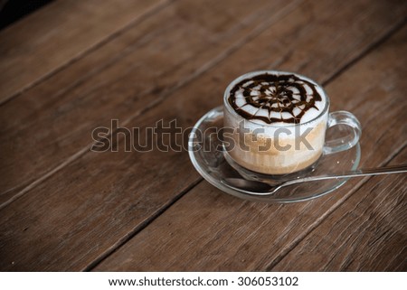 A cup of coffee with pattern in a glass cup on wooden background