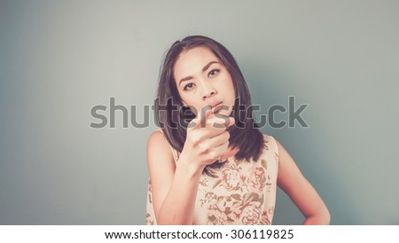Pointing on camera. Vintage, retro style of portrait of Asian woman in pink vintage dress on blue - green background.