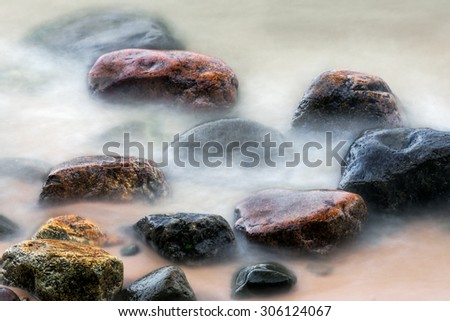 Shot with a long exposure time, colorful stones on a northern Michigan beach are surrounded by the ebb and flow of Lake Superior waves.
