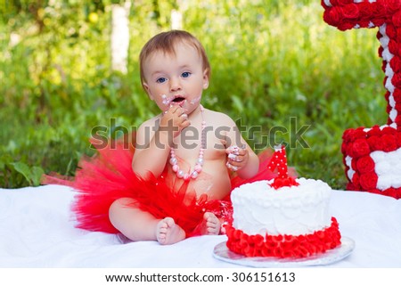 One year old girl sitting near celebration decorations and eating her first birthday cake