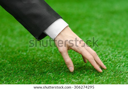 Nature and business topic: the hand of man in a black suit touching green grass