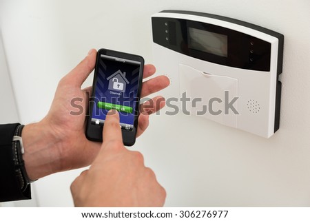 Close-up Of Businessperson Hands Arming Entrance Security System With Mobile Phone