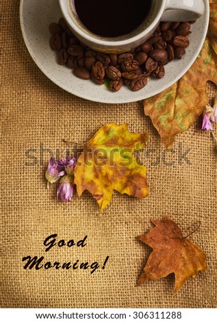 The label with words good morning and the cup of coffee with dry yellow maple leaves and everlasting flowers on sackcloth background