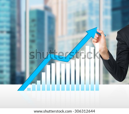 A hand is drawing a growing blue arrow as a concept of the success in business. Moscow cityscape in blur on the background.