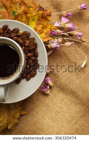 Tag with words hello autumn and the cup of coffee lying on the book with dry yellow maple leaves and everlasting flowers on sackcloth background