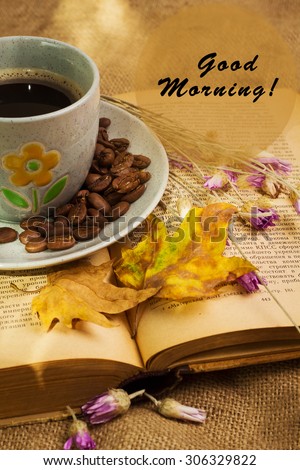 Banner with words good morning and the cup of coffee lying on the books with dry yellow maple leaves and everlasting flowers on sackcloth background