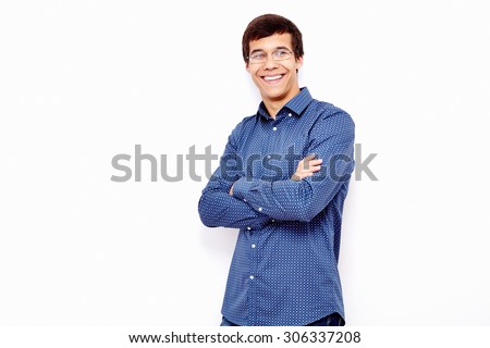 Young hispanic man wearing blue shirt and glasses standing with crossed arms and smiling against white wall