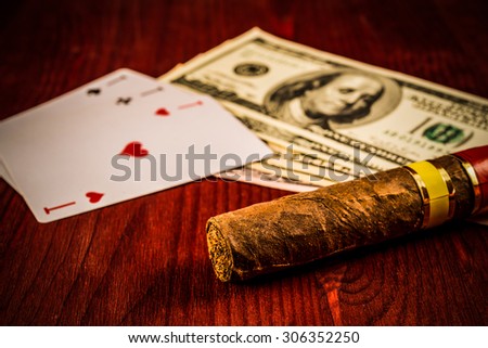 Cuban cigar with playing cards and money on the table mahogany. Focus on the cuban cigar, identification cards ace Russian letter, image vignetting and hard tones