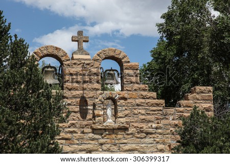 Beautiful tourism landmark historical 1930s Catholic church structure with old sign and symbol stone cross above cut stone wall and metal bell, in Quemado, New Mexico, USA