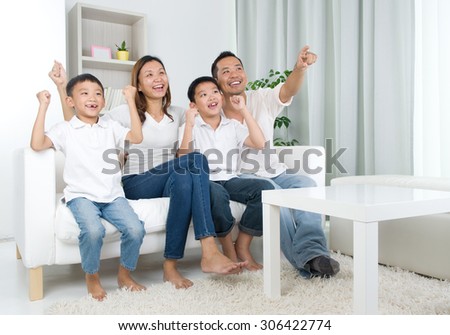Asian family watching television and shouting on their home side in a sporting competition Royalty-Free Stock Photo #306422774