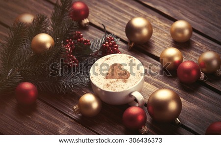 Cup of coffee with heart shape and christmas toys on wooden background.