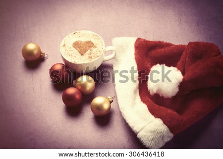 Cup of coffee with heart shape near Santas hat and christmas bubbles. Photo in old color image style.