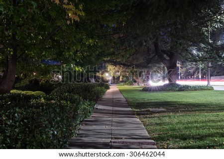 Residential, tree-lined neighborhood, with nobody walking on the sidewalk, and light trails from cars driving on street. Royalty-Free Stock Photo #306462044
