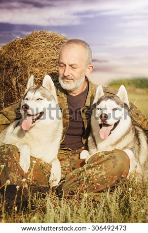 Farmer after a hard day's work. Old man with a beard sitting on a haystack with their dogs, enjoying summer sunset. Siberian Husky in the countryside. Harmony between man and nature.