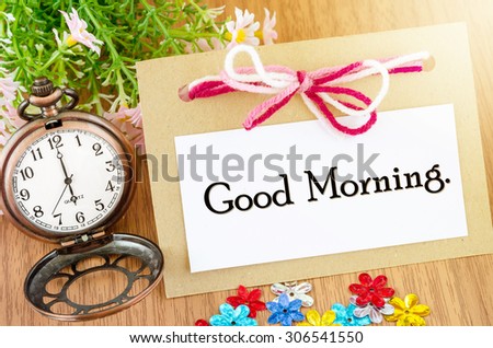 Good morning on paper tag and ribbon and pocket watch wite pink flower on wooden background.