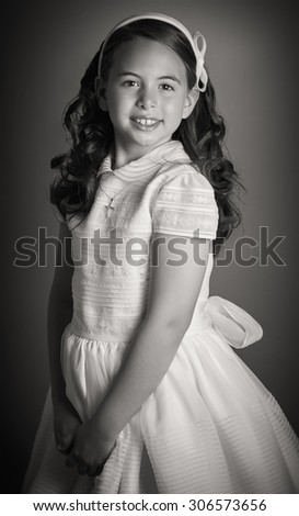 Beautiful young girl dressed in white. First Communion. Perfect teeth and smile, long curly hair, hands folded. Dark background, studio shoot. Sepia picture.