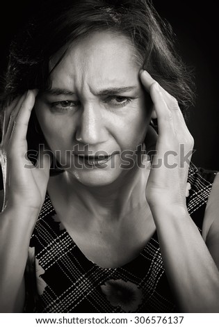 Close-up portrait of a middle aged woman with headache, massaging her forehead with both hands. Sepia picture, isolated on black.