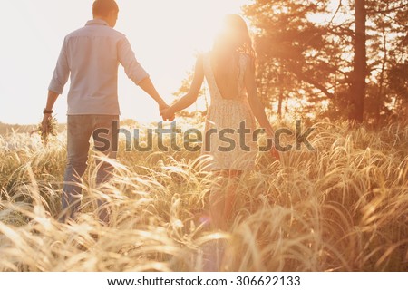 lovers walking in a field at sunset holding hands Royalty-Free Stock Photo #306622133