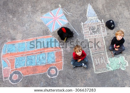 Two funny kid boys in british queen's guard soldier and policeman uniform having fun with London picture drawing with colorful chalks. With Big Ben, Union Jack and red bus.