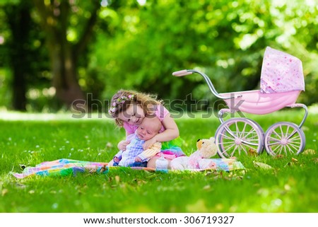Family with children enjoying picnic outdoors. Little girl playing with newborn baby brother in summer park. Child playing with toy stroller. Sister kissing new born sibling. Kids birthday party.