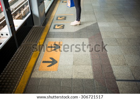 Woman feet stand in front of arrow sign at train station, Close up Arrow sign on floor at the sky train station, bangkok, Thailand