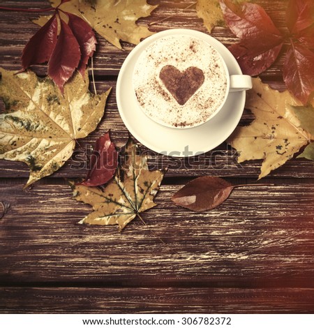 Autumn leafs and coffee cup on wooden table.
