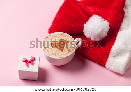 Cup of coffee with heart shape and christmas gift on pink background.