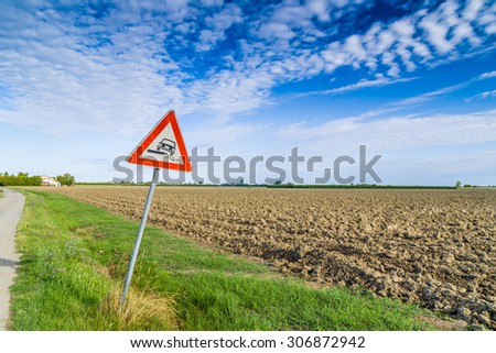 Hazardous Shoulder ruropean road sign along dirt road in Italian countryside on sky background