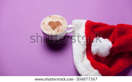 Cup of coffee and christmas hat on violet background.