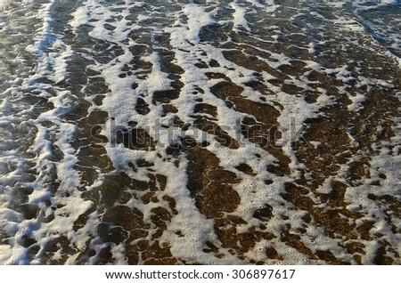 Foam pattern on sea surface over sand near seashore