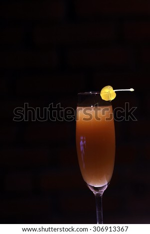 One glass with alcoholic mimosa or valencia cocktail of apricot liqueur orange juice sparkling dry wine and yellow cherry with stem on brick wall background, vertical photo