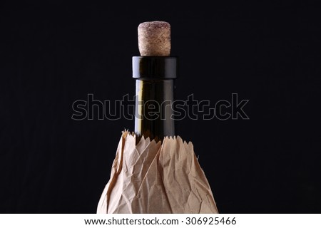 Closeup of one glass green wine corked bottle with alcohol beverage with cork in brown paper packet isolated on black studio background copyspace, horizontal picture