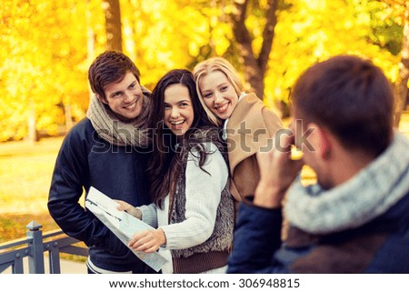 travel, people, tourism, photography and friendship concept - group of smiling friends with map taking picture in city park